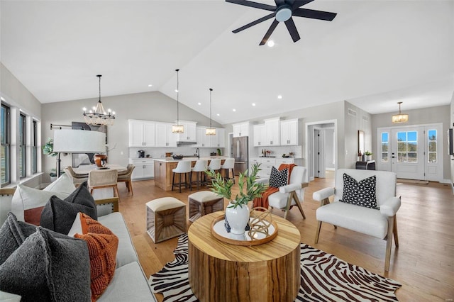 living room with light hardwood / wood-style floors, sink, high vaulted ceiling, and ceiling fan with notable chandelier