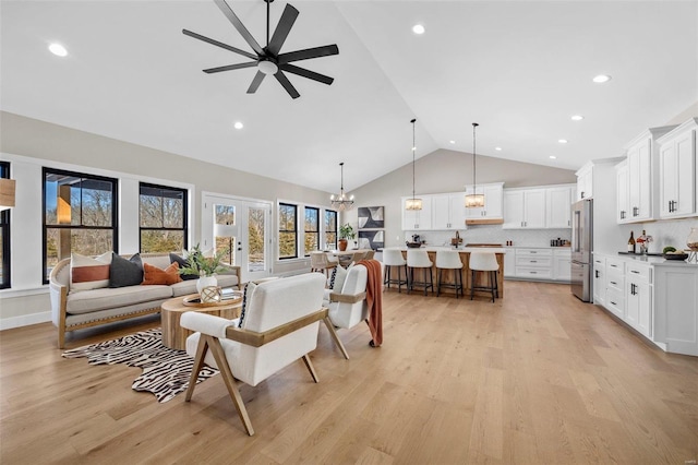 living room featuring light wood-type flooring, ceiling fan with notable chandelier, french doors, and high vaulted ceiling