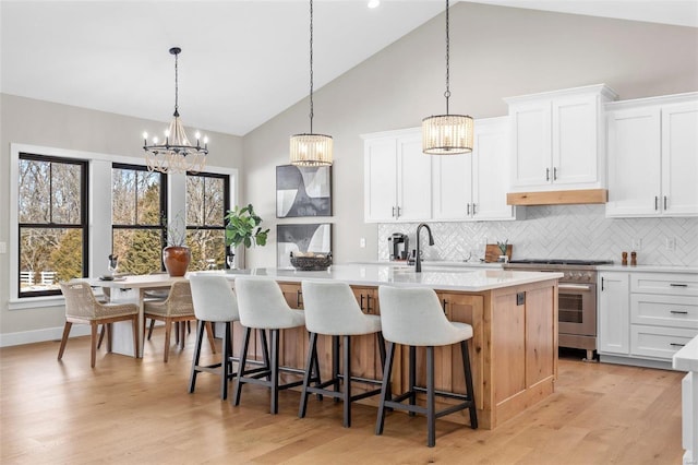 kitchen with stainless steel range, white cabinetry, a kitchen island with sink, and tasteful backsplash