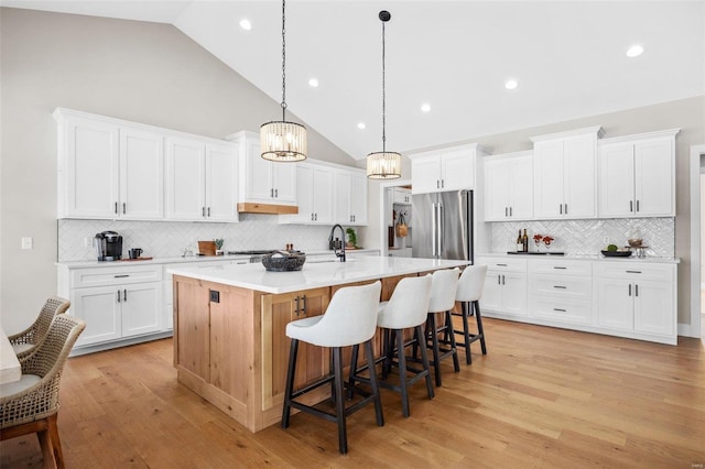 kitchen featuring hanging light fixtures, high end refrigerator, an island with sink, and white cabinetry