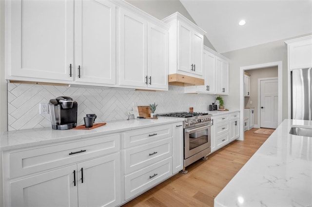 kitchen with vaulted ceiling, decorative backsplash, white cabinetry, stainless steel appliances, and light stone counters