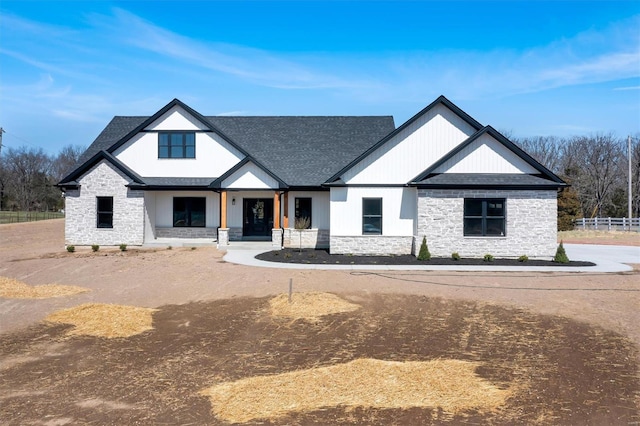 modern farmhouse with stone siding, a shingled roof, and fence