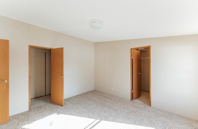 unfurnished bedroom featuring a closet, a walk in closet, and light colored carpet