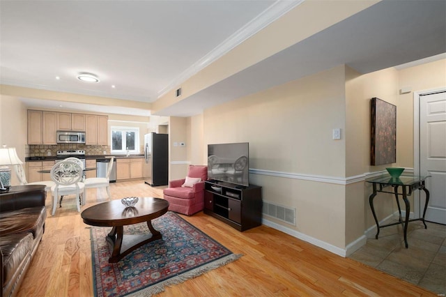 living room with light wood finished floors, baseboards, visible vents, and ornamental molding