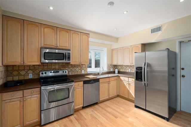 kitchen with stainless steel appliances, a sink, visible vents, light wood-style floors, and light brown cabinetry