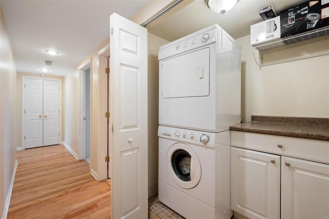 clothes washing area with stacked washer and dryer, baseboards, laundry area, and light wood finished floors