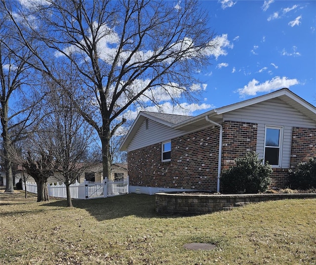 view of side of property featuring a yard, brick siding, and fence