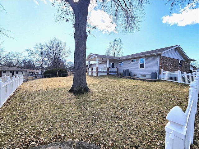 rear view of house with brick siding, central AC unit, a yard, and a fenced backyard