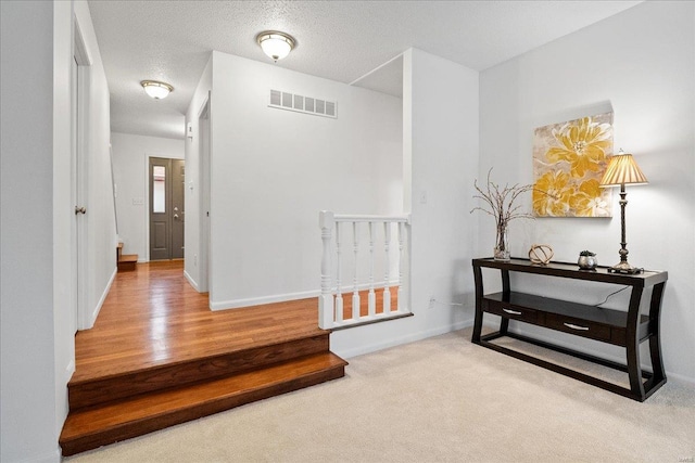 hallway featuring light colored carpet and a textured ceiling