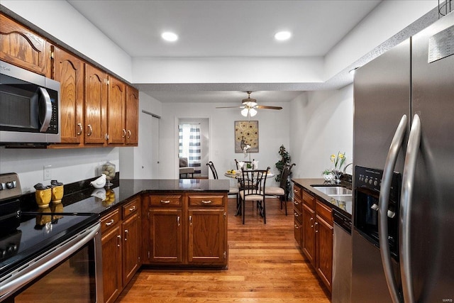 kitchen with light wood-type flooring, kitchen peninsula, sink, ceiling fan, and appliances with stainless steel finishes