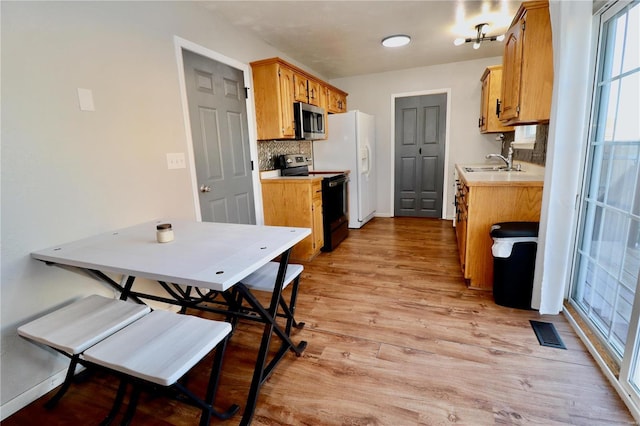 kitchen with tasteful backsplash, sink, stainless steel appliances, and light hardwood / wood-style flooring