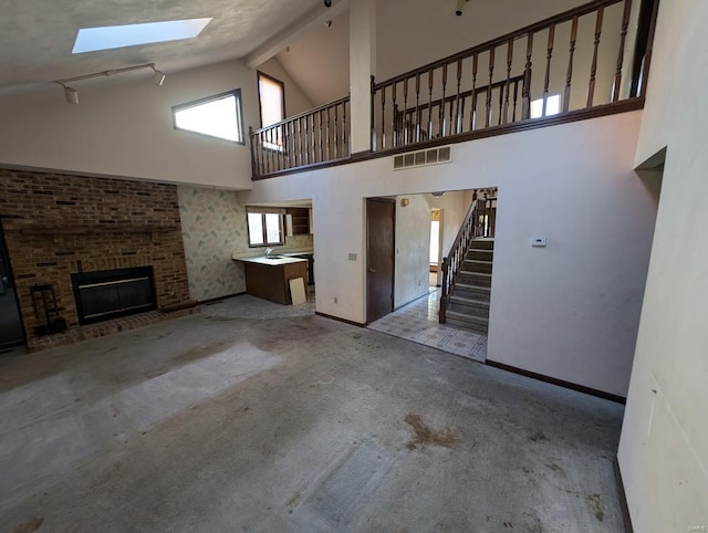 unfurnished living room featuring high vaulted ceiling, a skylight, and a fireplace