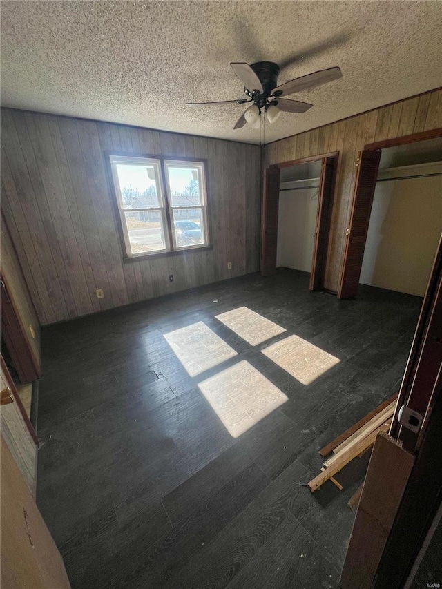 unfurnished bedroom with multiple closets, ceiling fan, and wood walls