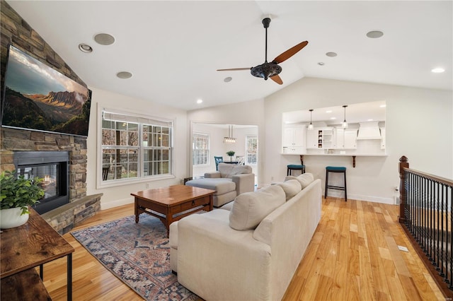 living room with vaulted ceiling, ceiling fan, a stone fireplace, and light hardwood / wood-style floors