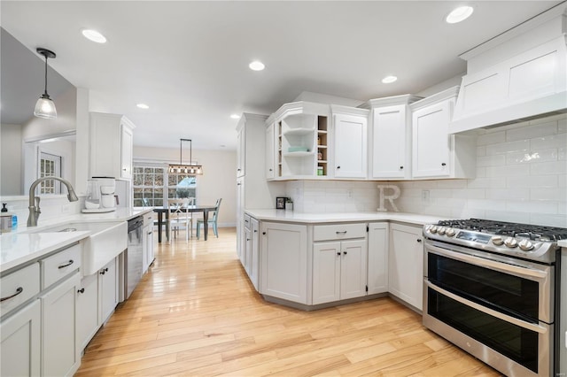 kitchen with appliances with stainless steel finishes, decorative light fixtures, white cabinetry, sink, and light hardwood / wood-style flooring