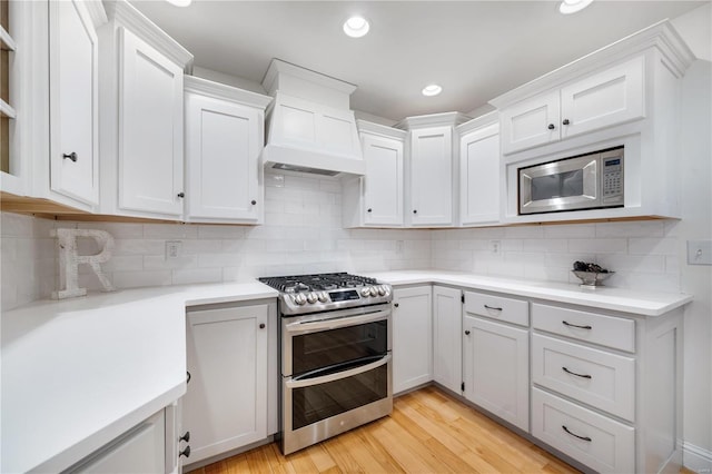 kitchen featuring premium range hood, light hardwood / wood-style flooring, stainless steel appliances, decorative backsplash, and white cabinets