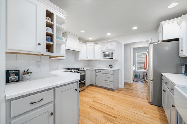 kitchen with appliances with stainless steel finishes, white cabinets, backsplash, and light hardwood / wood-style flooring