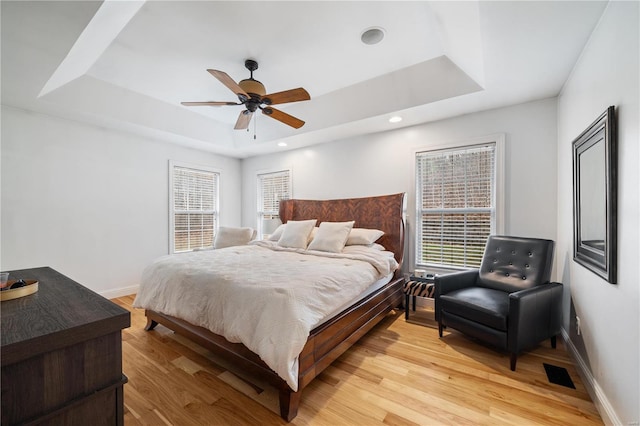 bedroom featuring light hardwood / wood-style flooring, ceiling fan, and a tray ceiling