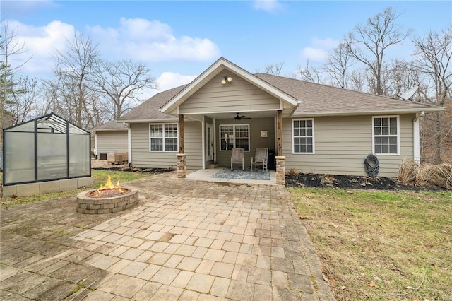 back of property with an outdoor structure, a patio, ceiling fan, and an outdoor fire pit