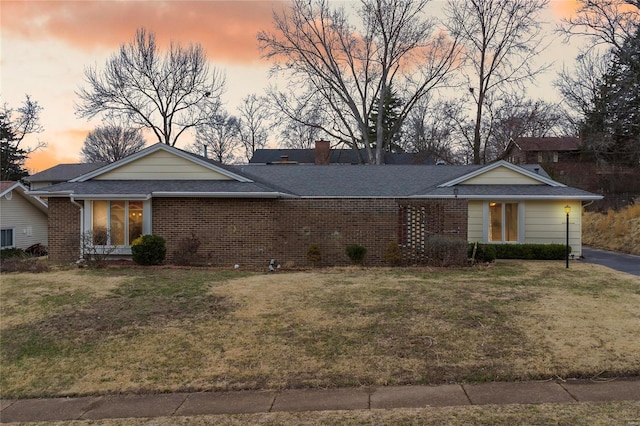 ranch-style home featuring brick siding, a shingled roof, and a front yard