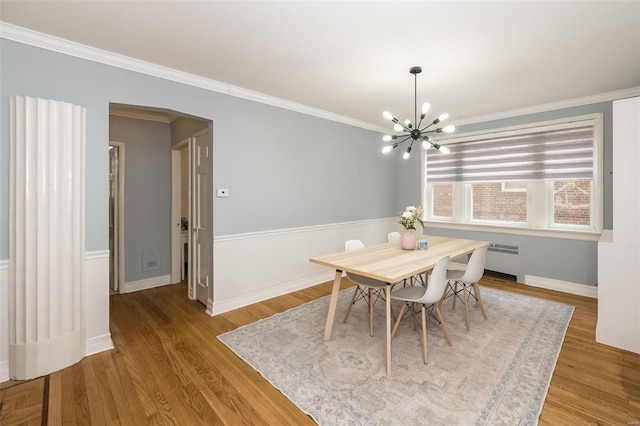 dining area featuring a notable chandelier, hardwood / wood-style flooring, radiator heating unit, and ornamental molding