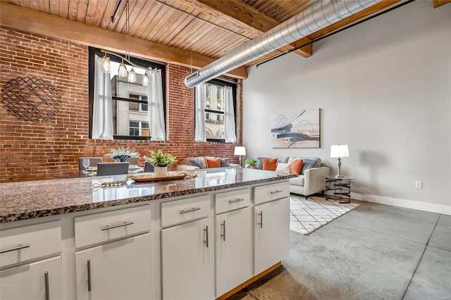 kitchen featuring wood ceiling, white cabinetry, beam ceiling, brick wall, and dark stone counters