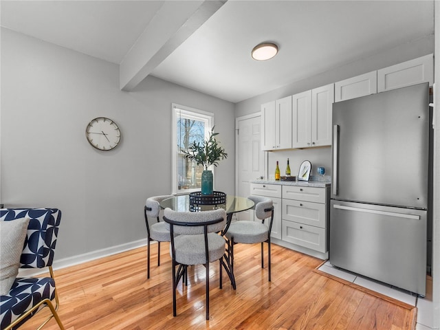 dining space with light wood-type flooring, beam ceiling, and baseboards