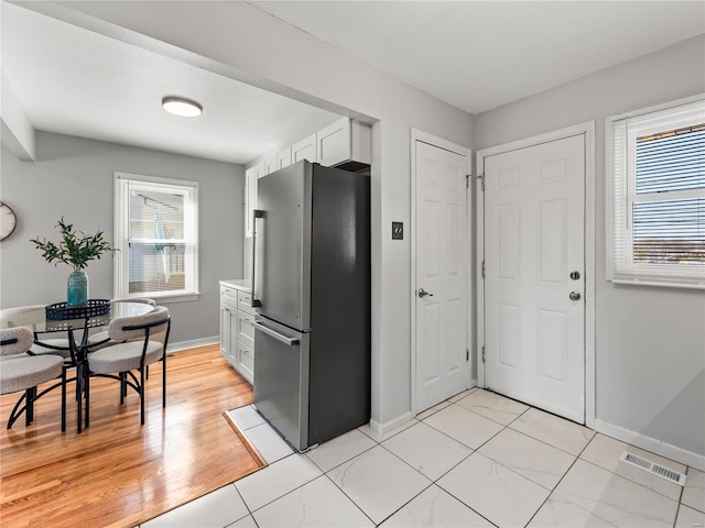 kitchen with visible vents, baseboards, white cabinets, light countertops, and freestanding refrigerator