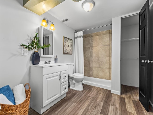 bathroom with visible vents, tiled shower, toilet, wood finished floors, and vanity