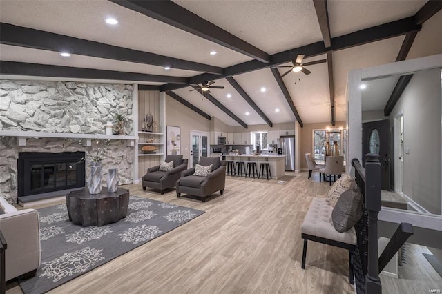 living room with vaulted ceiling with beams, a fireplace, light hardwood / wood-style flooring, and ceiling fan with notable chandelier