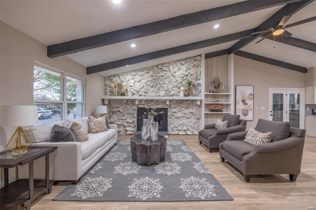 living room featuring ceiling fan, lofted ceiling with beams, a stone fireplace, and light hardwood / wood-style flooring