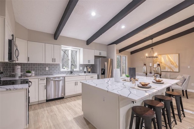 kitchen with white cabinets, a kitchen island, stainless steel appliances, vaulted ceiling with beams, and sink