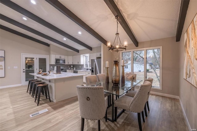 dining space with sink, light hardwood / wood-style flooring, lofted ceiling with beams, and an inviting chandelier