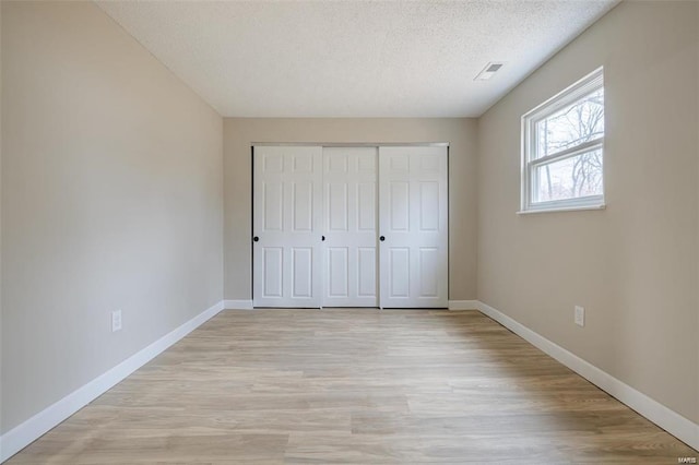 unfurnished bedroom featuring light wood-type flooring, a closet, and a textured ceiling