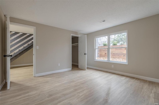 unfurnished bedroom featuring light hardwood / wood-style floors, a textured ceiling, a spacious closet, and a closet