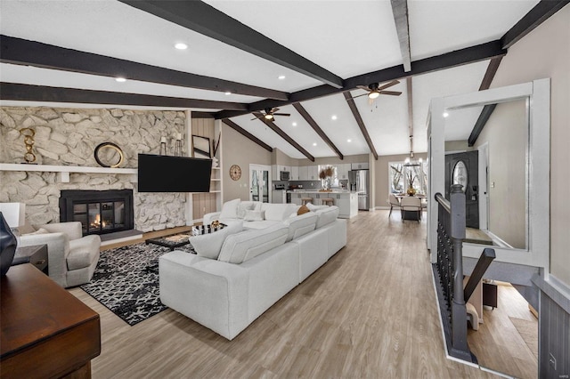 living room featuring light wood finished floors, a stone fireplace, ceiling fan with notable chandelier, and vaulted ceiling with beams