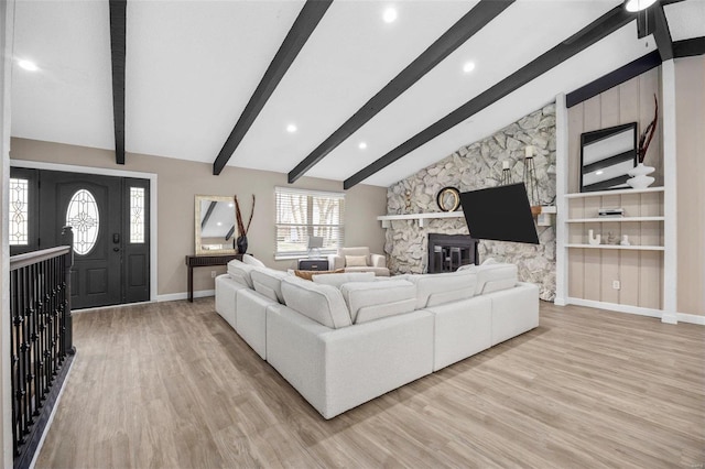 living area with baseboards, light wood-style floors, a stone fireplace, and vaulted ceiling with beams