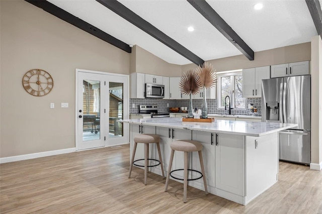 kitchen featuring tasteful backsplash, a kitchen island, lofted ceiling with beams, appliances with stainless steel finishes, and a kitchen breakfast bar