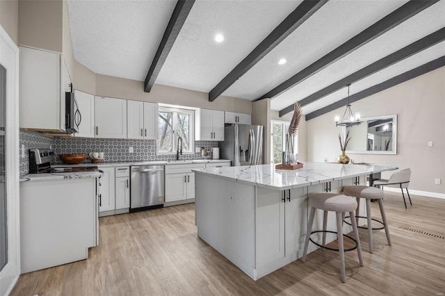 kitchen featuring lofted ceiling with beams, tasteful backsplash, a kitchen island, appliances with stainless steel finishes, and light stone countertops