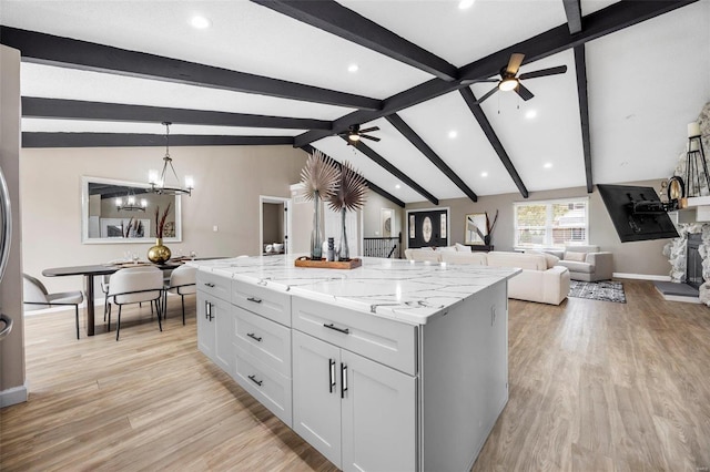 kitchen with light wood finished floors, a kitchen island, vaulted ceiling with beams, decorative light fixtures, and ceiling fan with notable chandelier