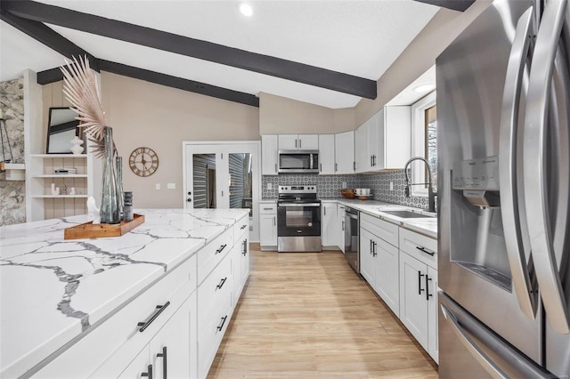 kitchen with a sink, light stone counters, lofted ceiling with beams, stainless steel appliances, and decorative backsplash