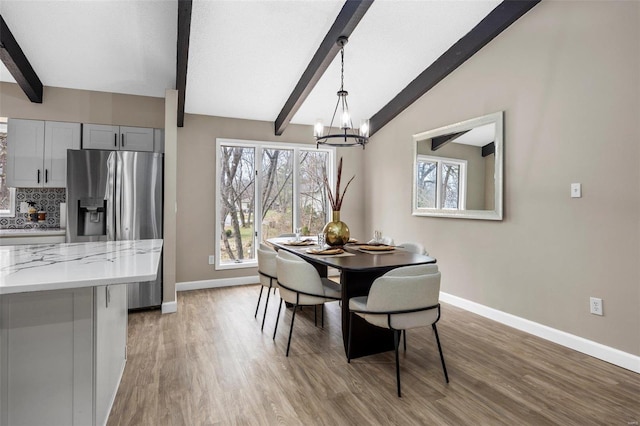 dining room with an inviting chandelier, light wood-style flooring, vaulted ceiling with beams, and baseboards