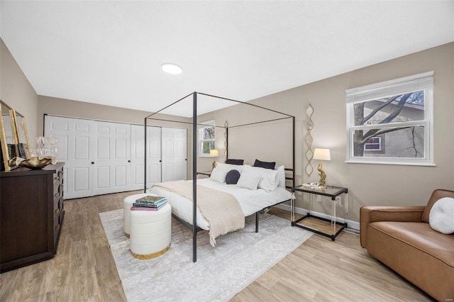 bedroom featuring light wood-style flooring, baseboards, and multiple closets