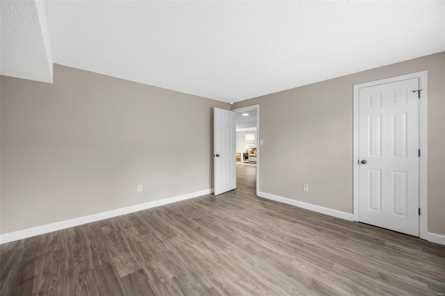 unfurnished bedroom featuring a textured ceiling, baseboards, and wood finished floors