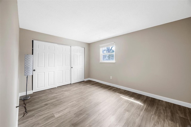 unfurnished bedroom featuring wood finished floors, baseboards, a closet, and a textured ceiling