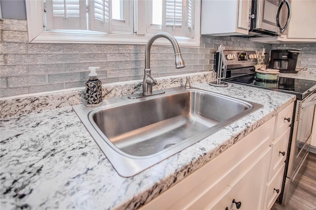 interior details with appliances with stainless steel finishes, sink, white cabinetry, light stone countertops, and decorative backsplash