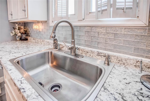 room details featuring light stone countertops, sink, white cabinets, and tasteful backsplash