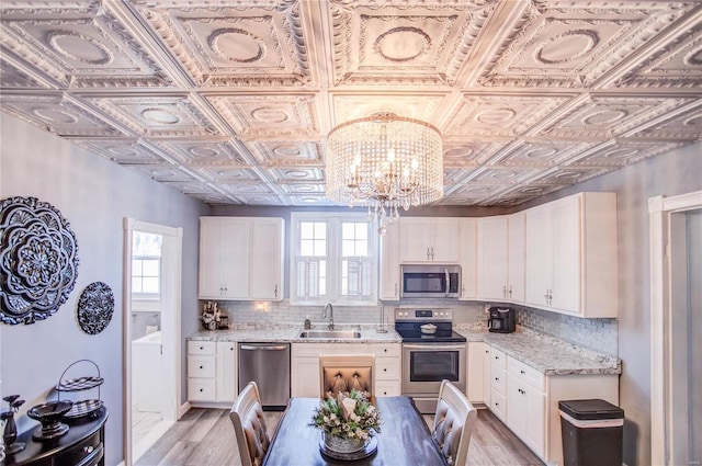 kitchen with appliances with stainless steel finishes, sink, white cabinetry, light stone counters, and decorative backsplash