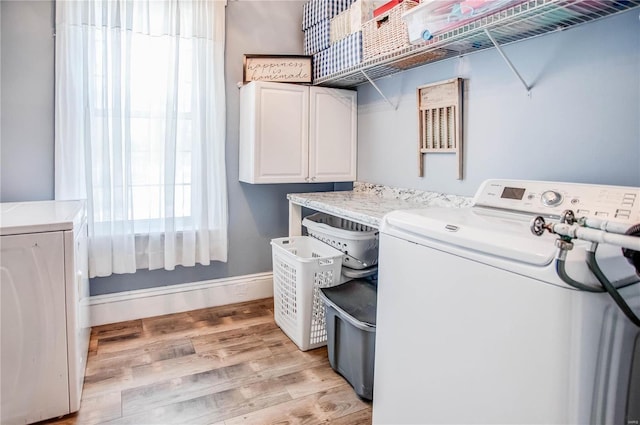 laundry area featuring washer and clothes dryer, light hardwood / wood-style floors, and cabinets