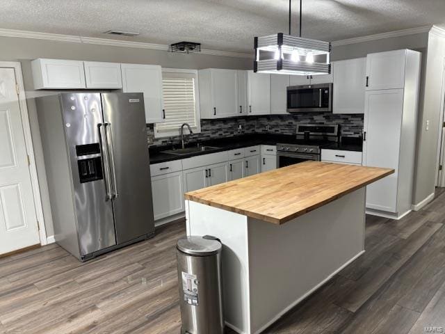 kitchen with butcher block counters, appliances with stainless steel finishes, hanging light fixtures, a kitchen island, and sink